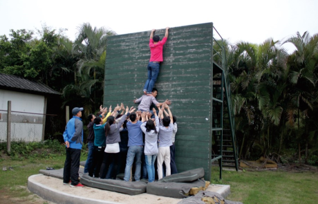 SKD employees working together to help a fellow employee scale a wall, exhibiting company culture